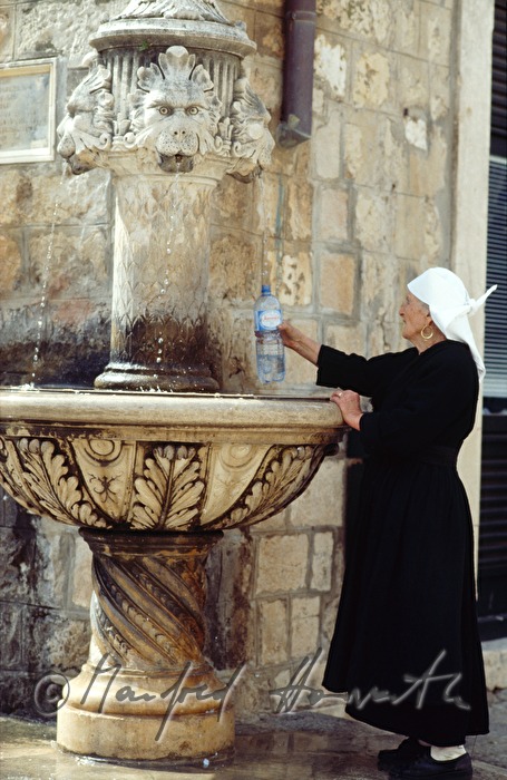 Frau nimmt Wasser von einem Brunnen