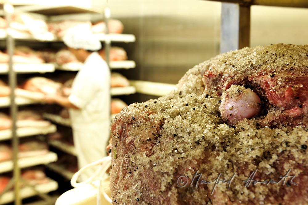 Fleischermeister prüft eingesalzene Schweineschlögel im Trockenraum